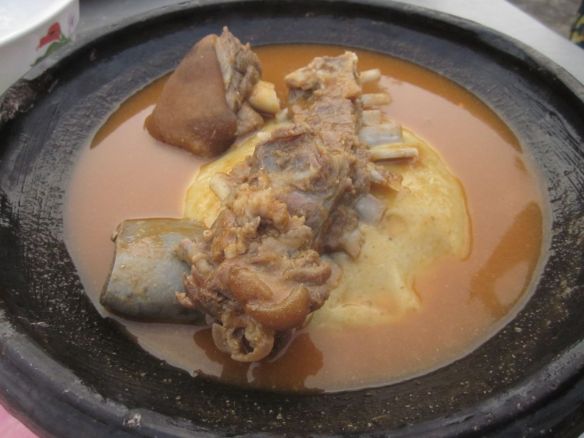 A bowl of stew with fufu in the middle and meat right on top